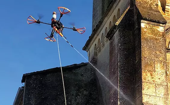 Un drone pulvérise de l’eau sur un bâtiment en pierre.